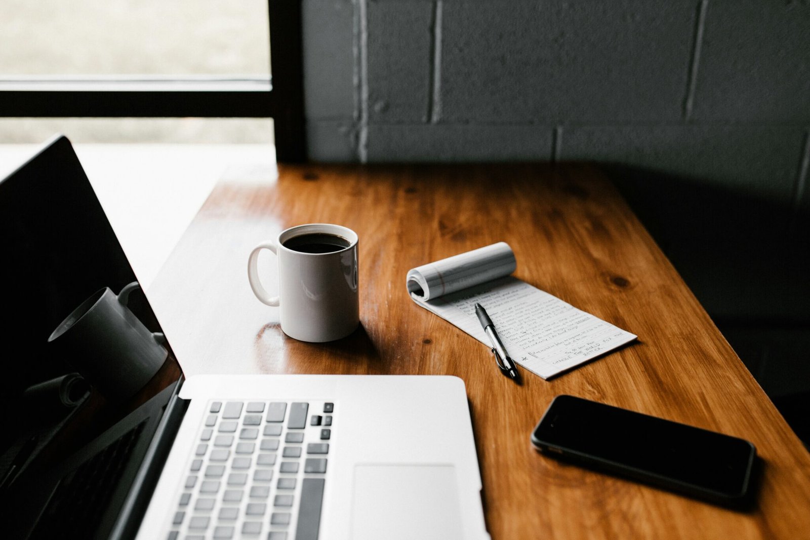 Mise en scène d'une prise de contact avec un bloc note, un ordinateur et un café posés sur un bureau dans un café